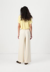 Yellow short-sleeve top, cream wide-leg pants with elastic waistband, and animal-print flats. Smooth fabric with minimal detailing.