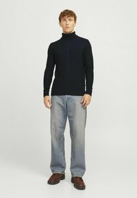 Pull en maille torsadée bleu marine avec un col roulé, associé à un jean droit à délavage clair et des chaussures chunky marron.