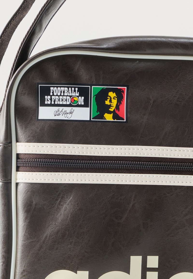 Borsa in pelle marrone scuro con cerniera bianca e toppa con la scritta "IL CALCIO È LIBERTÀ" accanto a un profilo a silhouette rosso, giallo e verde.