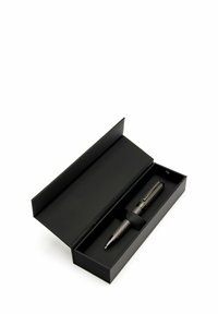 Stylo noir avec une finition métallique texturée à l'intérieur d'une boîte rectangulaire noire, maintenu en place par une sangle en tissu noir.