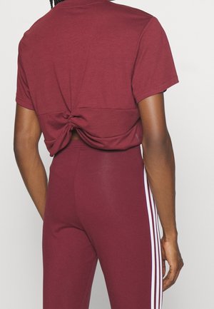 Osoba ubrana w bordowy, wiązany crop top i pasujące legginsy z wysokim stanem z białymi paskami po bokach, pokazana od tyłu.