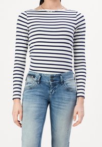 Gestreepte lange mouw top in marineblauw en wit, met een boot-hals. Gekoppeld aan lichtblauwe versleten jeans met twee knopen en voorkruiszakken.