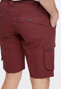 Maroon cargoshorts i lättviktsmaterial, med sid- och bakfickor med lockstängningar, samt kontrasterande svarta knappar.