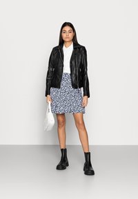 Zwarte leren jas over een witte blouse, gecombineerd met een blauwe bloemenrok. Zwarte enkellaarsjes en een witte handtas maken de look compleet.