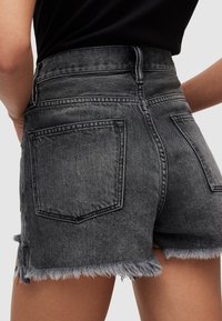 Pantalones cortos de mezclilla de cintura alta en lavado negro con dobladillo deshilachado, que cuentan con dos bolsillos traseros y detalles de costura en contraste.