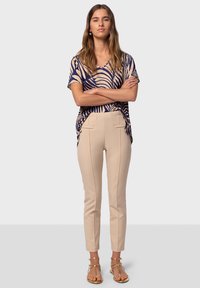 Haut ample bleu marine et beige à motifs avec des manches courtes, associé à un pantalon beige fuselé et des sandales dorées à lanières.