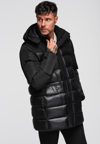 Giacca a vento nera con finitura lucida, cappuccio, tasche laterali e chiusura frontale con bottoni. Presenta un design trapuntato con cuciture a contrasto.