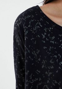 Top nero con un sottile motivo floreale scintillante, realizzato in materiale morbido con una vestibilità rilassata e scollatura ampia.