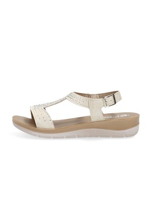Sandalia beige de punta abierta con tira en el tobillo, hebilla lateral, suela acolchada y pequeños tachones decorativos en la tira superior.
