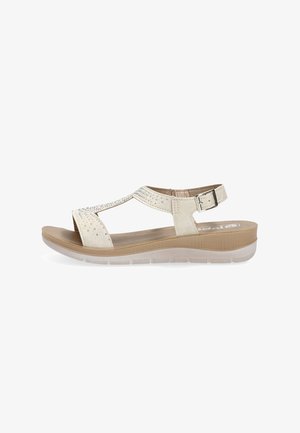 Sandalia beige de punta abierta con tira en el tobillo, hebilla lateral, suela acolchada y pequeños tachones decorativos en la tira superior.