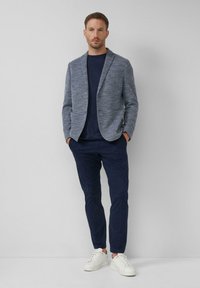 Marineblazer aus strukturiertem Stoff, kombiniert mit einem marineblauen T-Shirt und schlanken marineblauen Hosen. Die Schuhe sind weiße Sneaker.