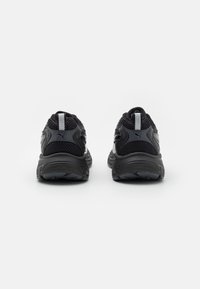 Black athletic shoes featuring a textured mesh upper, padded heel, and rubber outsole. Reflective accents on the back enhance visibility.