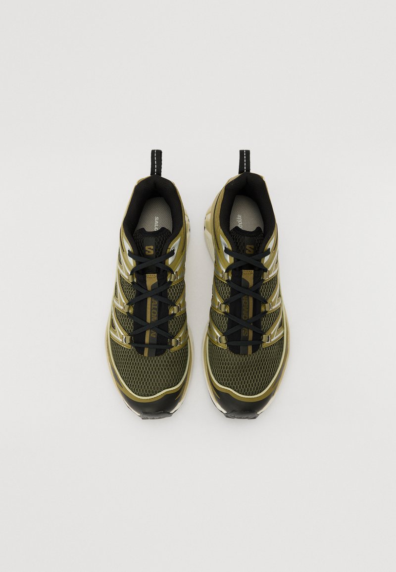 Olivgrüne Sportschuhe mit einem Obermaterial aus Mesh, schwarzen Schnürsenkeln und einer schwarzen Gummisohle. Verfügt über reflektierende Akzente und eine Zuglasche an der Ferse.