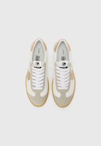 Hvite og beige sneakers med semsket tekstur, flate hvite snørebånd, gummisåle og en logopatch på siden. Rundt tådesign.