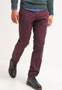 Pantaloni di cotone bordeaux con taglio slim, parte anteriore piatta e una sottile texture abbinati a scarpe in pelle nera, che presentano un classico design con lacci.