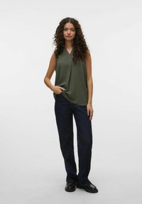 Un haut sans manches vert olive avec un col en V, associé à un jean large bleu foncé et des mocassins noirs, avec une texture subtile et une coupe décontractée.