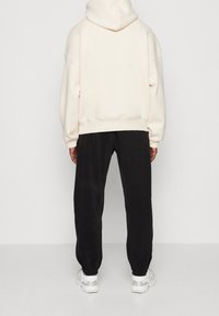 Felpa crema con cappuccio grande, polsini a coste e spalle scese, abbinata a pantaloni felpati neri e sneakers bianche, con motivi sottili.
