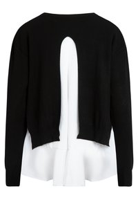 Pull noir à manches longues avec une fente dans le dos révélant un tissu blanc en dessous, créant un look superposé.