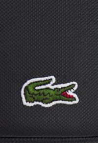 Tessuto nero con texture, decorato con un logo di coccodrillo verde, contornato con filo bianco e con accenti rossi sulla bocca.