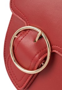 Borsa in pelle rossa con un grande accentuato anello dorato. Presenta dettagli cuciti e una texture liscia, che mette in risalto il suo design curvo.