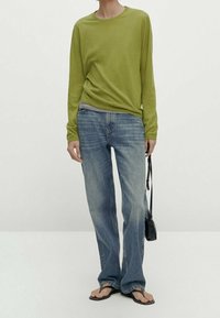 Długi rękaw, jasna zielona bluzka połączona z jasnoniebieskimi jeansami o prostych nogawkach. Obuwie: czarne klapki. Dodatek: mała czarna torebka na ramię.