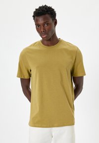 Oliven grøn bomulds t-shirt med korte ærmer, rund halsudskæring og en afslappet pasform. Glat tekstur, minimal syning.