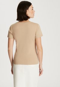 Beżowa koszulka z krótkim rękawem z gładkiego materiału, z klasycznym okrągłym dekoltem i dopasowanym krojem, noszona z białą spódnicą.