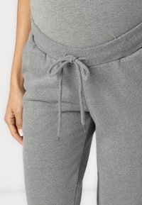 Pelēki sporta bikses, kas izgatavotas no mīkstas kokvilnas. Tām ir elastīga josta ar auklu un sānu kabatām. Gluda tekstūra kopumā.