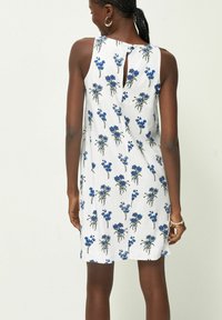 Blommig klänning med vit bakgrund och blommönster i blått, ärmlös design och nyckelhålöppning bak.