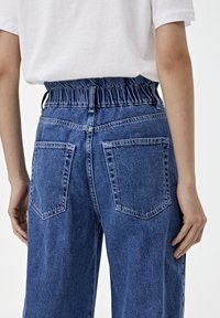 Jeans de denim azul con una banda elástica en la cintura, corte relajado y dos bolsillos traseros, con una textura desteñida y detalles de costura.