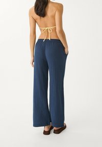Pantalon large marine en tissu texturé avec taille à cordon de serrage, doté de poches latérales et d'une coupe décontractée.