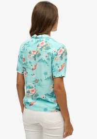Koszula z krótkim rękawem w jasnoniebieskim materiale z tropikalnym kwiatowym wzorem, z akcentami palm i kolorowymi elementami.