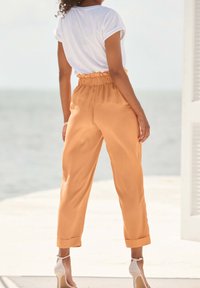Saténové kalhoty s vysokým pasem v jemné oranžové barvě, s nařaseným pasem a manžetami, kombinované s jednoduchým bílým topem s krátkým rukávem.