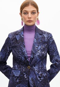 Lila und schwarze Tierdruck-Blazer mit einem einzelnen goldenen Knopf, mit taillierter Passform und strukturiertem Stoff. Getragen über einem passenden hoch geschnittenen Oberteil.