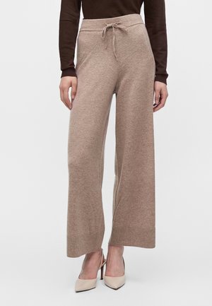 Mannequin portant un pantalon large en maille taupe avec une taille à cordon et des talons pointus beige.