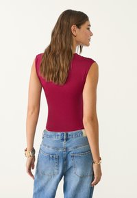 Burgunderfarbener, taillierter Body mit kurzen Ärmeln, kombiniert mit hochtaillierten, hellblauen Jeans aus Denim. Weicher Stoff und minimalistische Designmerkmale.