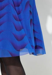 Robe en maille bleue avec des motifs violets ondulés, silhouette fluide et ourlet au milieu du mollet. Le tissu semble léger et semi-transparent.