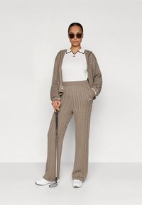 Brown knitted hoodie and matching trousers with a cable pattern. White collared shirt underneath, paired with dark sunglasses and golf club.
