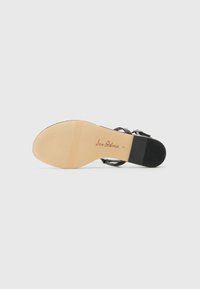 Sorte hællet sandal med et glat læderoverdel, en slank ankelrem og en beige sål. Har et diskret branding-aftryk på sålen.