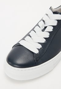 Gros plan d'une basket en cuir noire avec de larges lacets blancs et une semelle épaisse en caoutchouc blanc sur fond blanc.