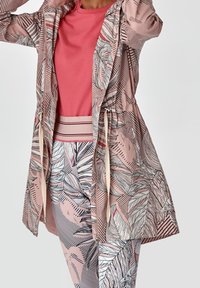 Różowo-beżowa kurtka z wzorami liści, ześciągnięta w talii, z trokami, na różowej koszulce. Legginsy z wzorem liści, podobnym do tego na kurtce.