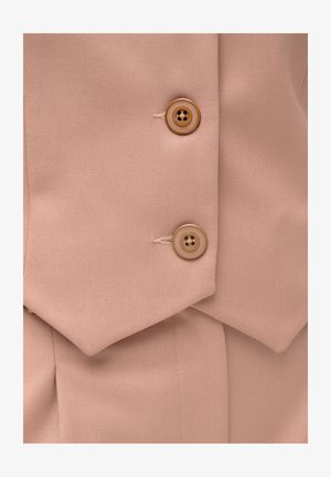 Zbliżenie na beżową tkaninę z dwoma jasno-brązowymi guzikami przyszytymi na nakładających się klapach dopasowanego ubrania.