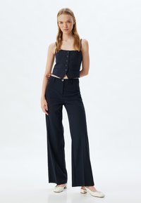 Navy blue cropped vest with vertical pinstripes and front buttons, paired with high-waisted, wide-leg trousers in matching color.