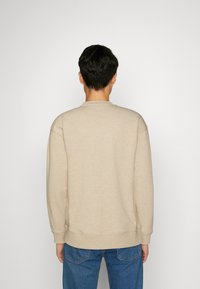 Sweatshirt beige con polsini e orlo a coste, caratterizzato da un classico scollo a girocollo. Il tessuto appare morbido e leggermente texturizzato.