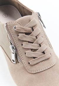 Zapato de ante beige con punta redonda, que cuenta con cordones y una cremallera funcional en el lateral, con un acabado texturizado y sutiles detalles de costura.