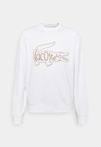 Sweatshirt blanc en mélange de coton, avec un grand logo crocodile beige accompagné du texte "Lacoste", col rond et poignets côtelés.