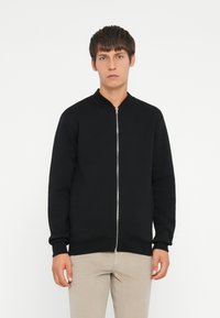 Sort zip-up bomberjakke med en rund krave, lange ærmer, ribbede manchetter og kant, lavet af et glat, let tekstureret stof.