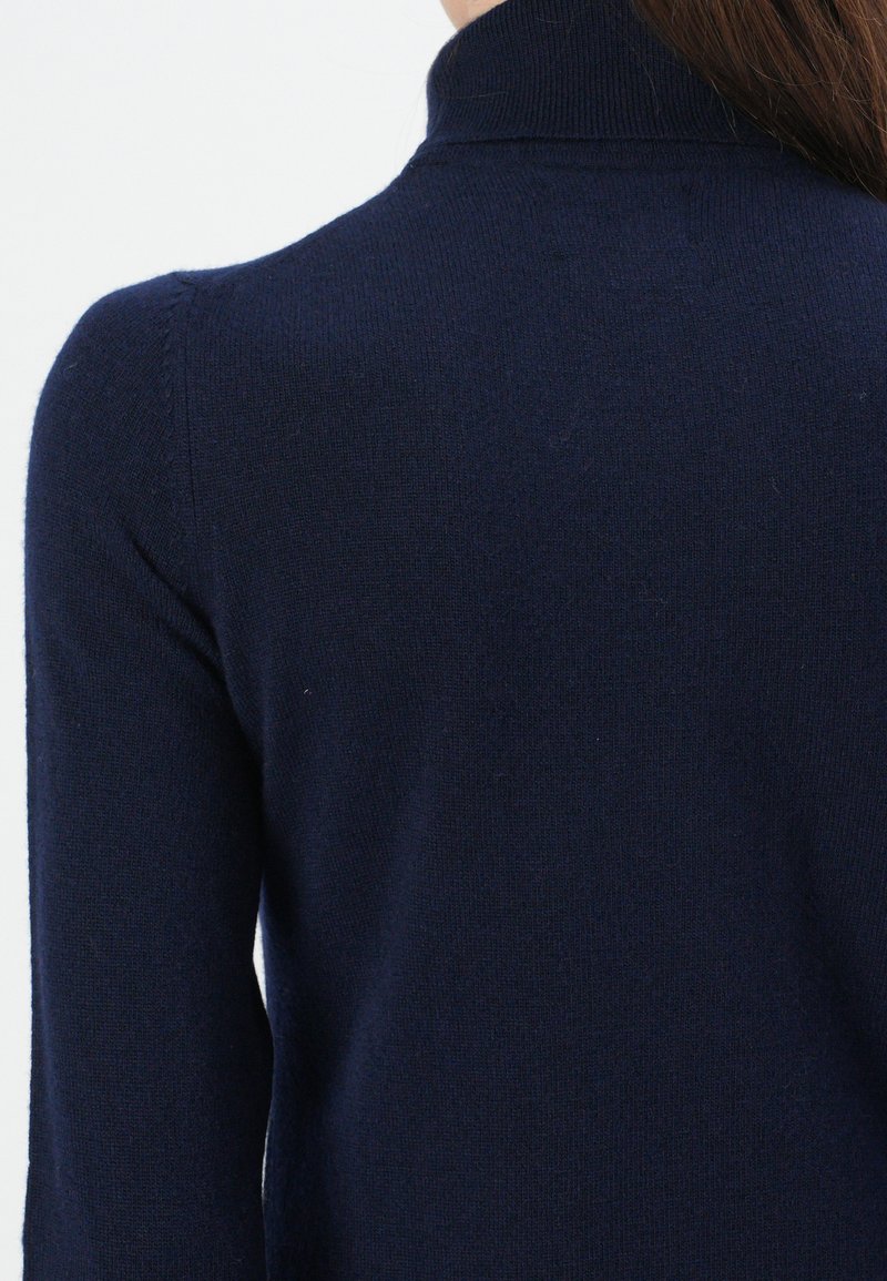 Person, der einen navyblauen, langärmligen, gerippten Rollkragenpullover trägt, von hinten und über die Schultern gesehen.