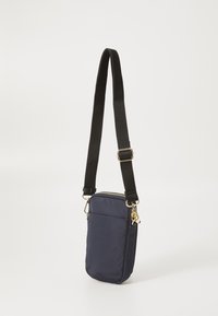 Sac bandoulière en nylon bleu marine avec une forme rectangulaire mince, doté d'un compartiment zippé en haut, d'une poche avant et d'une sangle noire réglable avec des accessoires en or.