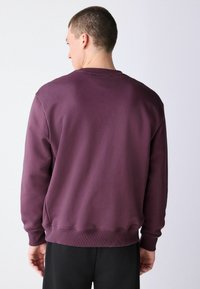 Bordó pulóver kerek nyakkal, bordázott mandzsettákkal és szegéllyel. Simaságú anyag, enyhén bő fazon, látható minta vagy grafika nélkül.